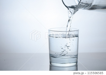 Drinking water is poured into a glass from a jug Drinking water is poured into a glass from a jug 115506585