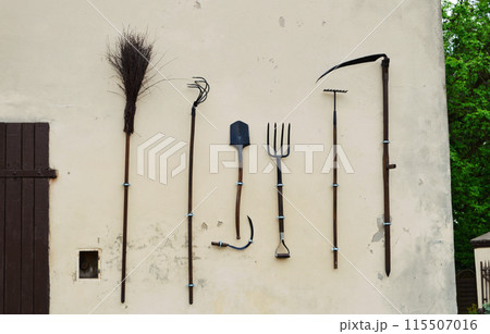 On the wall of the shed hangs a set of gardening tools. 115507016