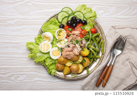 Nicoise salad with tuna, eggs, potatoes, green beans, and olives on a white table 115510928