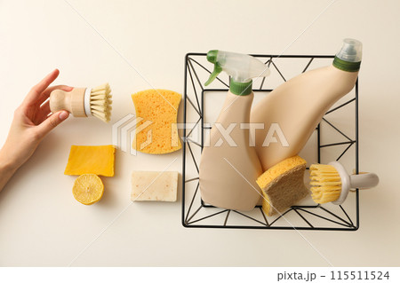 Bottles with detergent in basket, soap, brushes in hand and sponges on beige background, top view Bottles with detergent in basket, soap, brushes in hand and sponges on beige background, top view 115511524