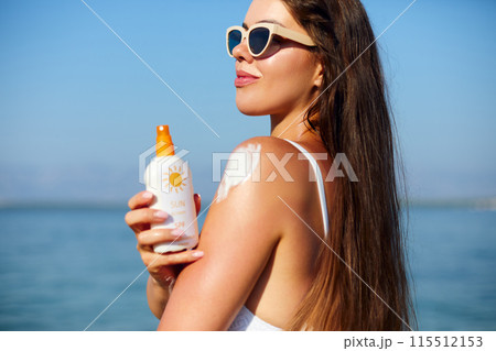 Woman putting sunblock lotion on shoulder before tanning during summer holiday on beach. Sun cream. Suntan. Beautiful Woman Applying Sunscreen Solar Cream. Skin care. Sun protection Woman putting sunblock lotion on shoulder before tanning during summer holiday on beach. Sun cream. Suntan. Beautiful Woman Applying Sunscreen Solar Cream. Skin care. Sun protection 115512153