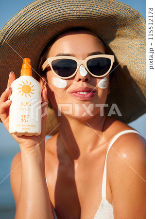 Beautiful Young woman with sun cream on face. Girl holding sunscreen bottle on the beach. Female in hat applying moisturizing lotion on skin.Skin care. Sun protection. Suntan Beautiful Young woman with sun cream on face. Girl holding sunscreen bottle on the beach. Female in hat applying moisturizing lotion on skin.Skin care. Sun protection. Suntan 115512178