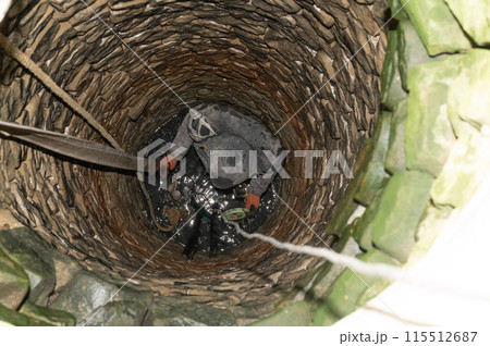 A man in the middle of a well cleans the bottom of dirt and accumulated silt. 115512687