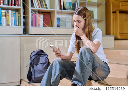 Sad teenage girl student looking at smartphone screen inside high school classroom Sad teenage girl student looking at smartphone screen inside high school classroom 115514989