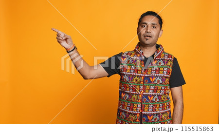 Salesman pointing around with finger, doing recommendation, talking with audience. Indian person showing copy text, doing advertisement, isolated over studio background, camera B Salesman pointing around with finger, doing recommendation, talking with audience. Indian person showing copy text, doing advertisement, isolated over studio background, camera B 115515863
