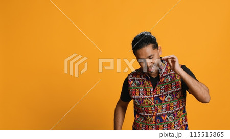 Smiling person having fun, dancing on rhythm, enjoying relaxation time. Jolly indian man goofing around, entertaining himself doing funky movements, isolated over studio background, camera A Smiling person having fun, dancing on rhythm, enjoying relaxation time. Jolly indian man goofing around, entertaining himself doing funky movements, isolated over studio background, camera A 115515865