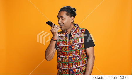 Irked indian man fighting with friends during telephone call, isolated over studio background. Outraged person arguing with mates during conversation on mobile phone, camera B 115515872