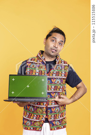 Portrait of tech professional pointing finger towards green screen laptop, isolated over studio backdrop. Content creator doing technology reviews, presenting mockup notebook 115515886