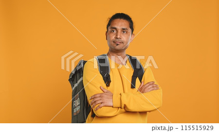 Portrait of upbeat indian man holding thermal backpack, isolated over studio background. Friendly cheerful person prepared to deliver takeaway food to customers, camera A Portrait of upbeat indian man holding thermal backpack, isolated over studio background. Friendly cheerful person prepared to deliver takeaway food to customers, camera A 115515929