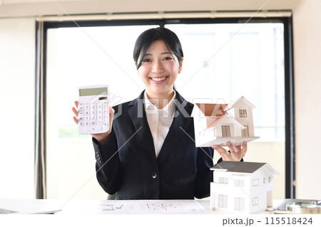 住宅模型と電卓を持つスーツ姿の若い女性 115518424