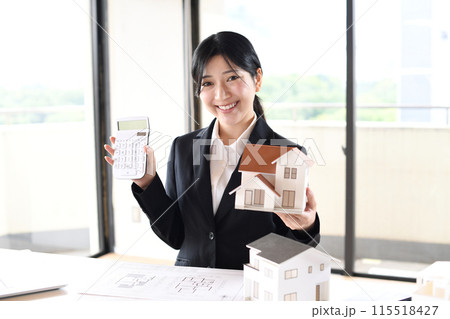 住宅模型と電卓を持つスーツ姿の若い女性 115518427