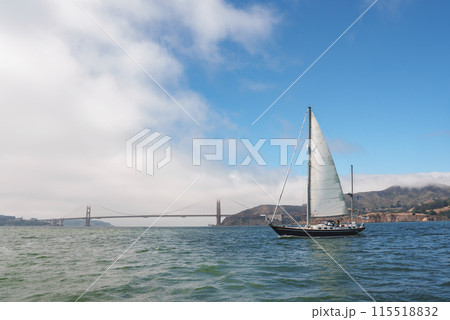 Enjoy a serene maritime view with the iconic Golden Gate Bridge in San Francisco. A yacht glides gracefully with hoisted sails on calm waters, under a clear sky. Enjoy a serene maritime view with the iconic Golden Gate Bridge in San Francisco. A yacht glides gracefully with hoisted sails on calm waters, under a clear sky. 115518832