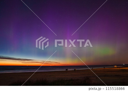 A mesmerizing aurora borealis display with vibrant purple, green, and blue hues over Jurmala beach in Latvia. The calm sea reflects the colors, enhancing the scene. 115518866