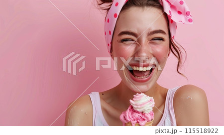 Cheerful young woman with a pink polka-dot headband laughing and enjoying a pink and white ice cream cone against a pink background. 115518922