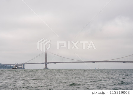 Tranquil view of Golden Gate Bridge in San Francisco, CA. Overcast sky, calm water, boat for scale. Serene simplicity of iconic bridge against muted colors. 115519008