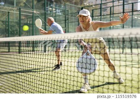 Mature sporty woman playing padel game in court on sunny day 115519376