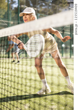 Motivated senior woman playing padel with her teammate in court Motivated senior woman playing padel with her teammate in court 115519409
