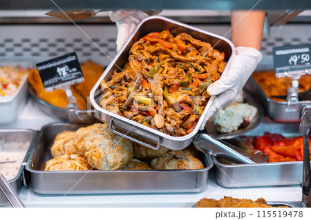 Salesman lays out a tray of pieces of lamb with noodles and vegetables on supermarket display window Salesman lays out a tray of pieces of lamb with noodles and vegetables on supermarket display window 115519478