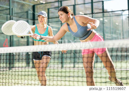 Two young sporty girls playing padel game in court on sunny day Two young sporty girls playing padel game in court on sunny day 115519607