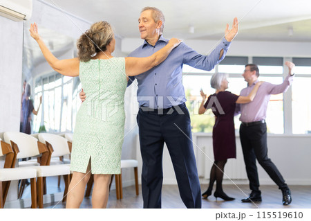 Active elderly couple in their free time is engaged in latin dance class and learns movements of cha-cha-cha dance Active elderly couple in their free time is engaged in latin dance class and learns movements of cha-cha-cha dance 115519610