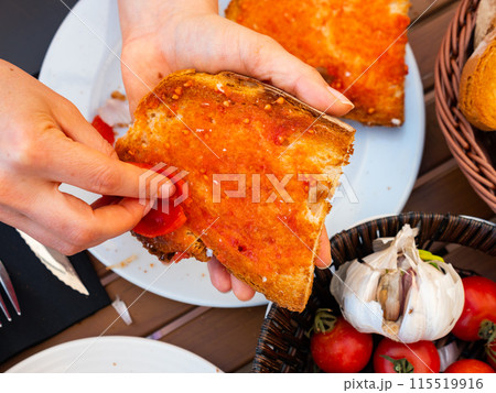 Female hands rubbing toast with tomato while preparing Pan Con Tomate 115519916