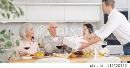 Birthday senior man accepts outright gift and greetings from adult son during family feast 115520526