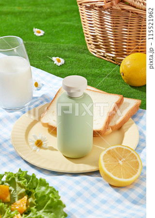 Creative photo from above view, a blue picnic rug with checkered pattern spread on the green grass, a few dishes, a glass of milk and a green unlabeled bottle placed above. Copy space for adding text Creative photo from above view, a blue picnic rug with checkered pattern spread on the green grass, a few dishes, a glass of milk and a green unlabeled bottle placed above. Copy space for adding text 115521962