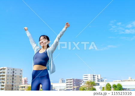 青空に向かってガッツポーズする若い女性　ダイエット　街中　解放　正面 115523310