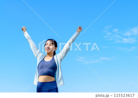 青空に向かってガッツポーズする若い女性　ダイエット　街中住宅街　解放　正面　空メイントリミングアップ 115523617