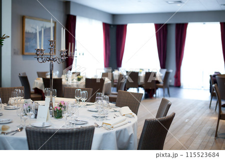 Elegant restaurant with round tables, candle holders, creating a cozy and classy dining atmosphere Elegant restaurant with round tables, candle holders, creating a cozy and classy dining atmosphere 115523684
