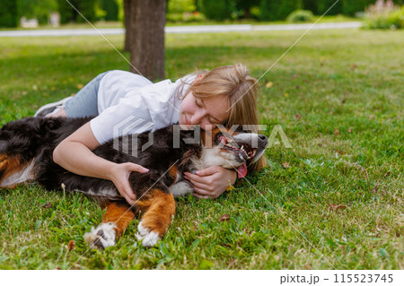 A woman and a black dog bonding on grass in a sunny park, showing friendship and happiness outdoors A woman and a black dog bonding on grass in a sunny park, showing friendship and happiness outdoors 115523745