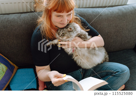 middle-aged woman sits on sofa by window with cat middle-aged woman sits on sofa by window with cat 115525080