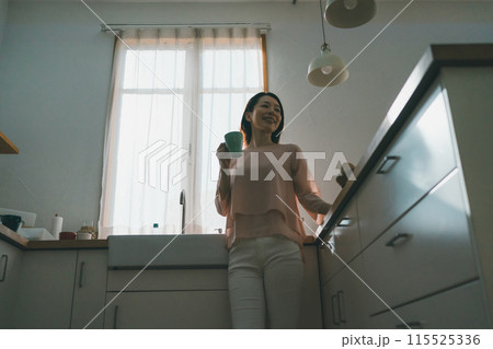 キッチンでマグカップを持ってリラックスしている40代女性 115525336