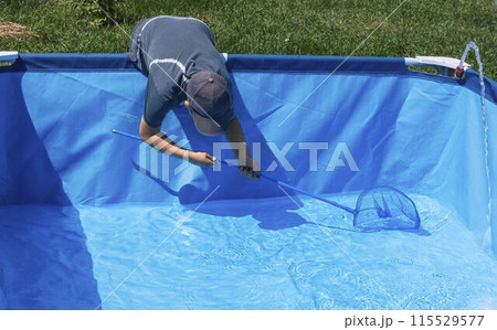 Boy diligently skimming leaves and debris from a sparkling blue pool, illustrating the routine upkeep required to maintain clarity and cleanliness 115529577