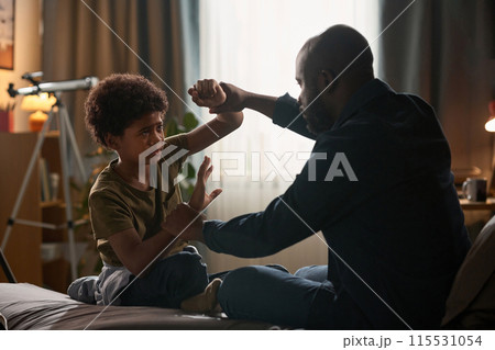 Side view portrait of father and son fighting aggressively sitting on bed in dramatic light copy space 115531054