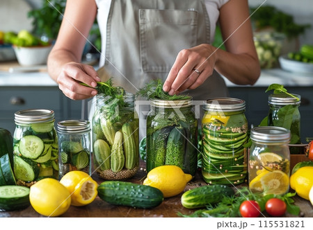 Woman Adding Dill to Homemade Cucumber Pickles in Kitchen 115531821