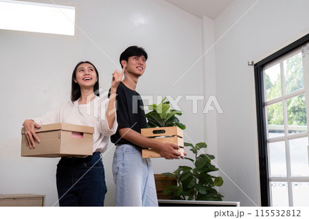 Happy Couple Moving into New House with Boxes and Plants, Excited About New Home, Bright Modern Interior, Natural Light, Fresh Start, Young Adults, Homeownership, Relocation, Lifestyle Change 115532812