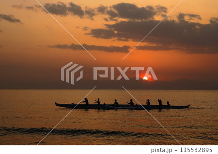夕暮れの逗子海岸、オレンジ色に染まる海でボートの練習をする若者達のシルエット 夕暮れの逗子海岸、オレンジ色に染まる海でボートの練習をする若者達のシルエット 115532895