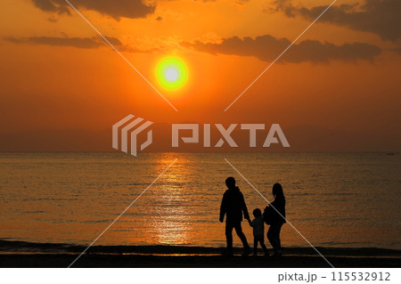 オレンジ色に染まる夕暮れの逗子海岸、波打ち際を散歩する家族のシルエット 115532912