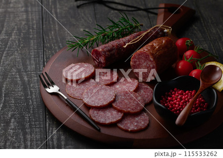 カッティングボードの上にのせた熟成サラミ　ピンクペッパーとローズマリーとプチトマトとレモン 115533262