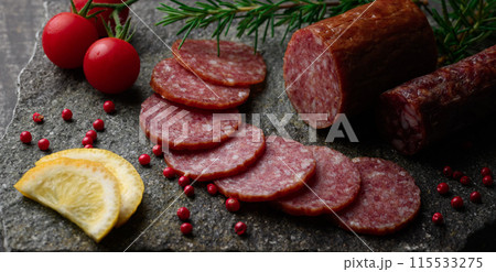カッティングボードの上にのせた熟成サラミ ピンクペッパーとローズマリーとプチトマトとレモン カッティングボードの上にのせた熟成サラミ ピンクペッパーとローズマリーとプチトマトとレモン 115533275