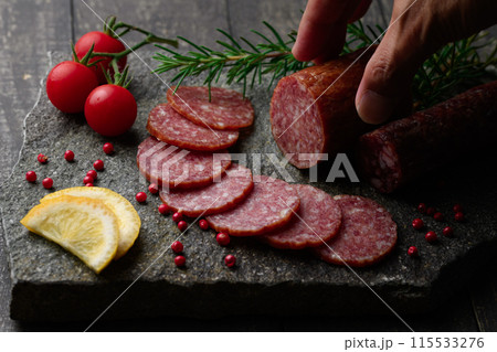 カッティングボードの上にのせた熟成サラミ　ピンクペッパーとローズマリーとプチトマトとレモン 115533276