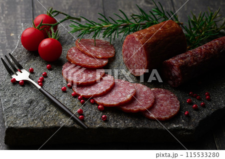 カッティングボードの上にのせた熟成サラミ ピンクペッパーとローズマリーとプチトマトとレモン カッティングボードの上にのせた熟成サラミ ピンクペッパーとローズマリーとプチトマトとレモン 115533280