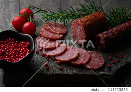 カッティングボードの上にのせた熟成サラミ ピンクペッパーとローズマリーとプチトマトとレモン カッティングボードの上にのせた熟成サラミ ピンクペッパーとローズマリーとプチトマトとレモン 115533286