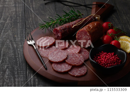 カッティングボードの上にのせた熟成サラミ　ピンクペッパーとローズマリーとプチトマトとレモン 115533309