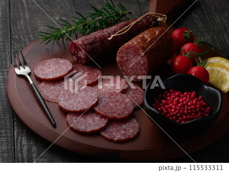 カッティングボードの上にのせた熟成サラミ ピンクペッパーとローズマリーとプチトマトとレモン カッティングボードの上にのせた熟成サラミ ピンクペッパーとローズマリーとプチトマトとレモン 115533311