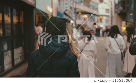 Caucasian woman walking evening Tokyo streets. Attractive girl tourist travel Japan landmark enjoys city vibe in holiday vacation. Street fashion, night life. Back view 115535064