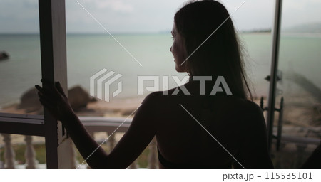 Beautiful girl relax on resort bungalow terrace with ocean view on holiday summer vacation. Tropical island sea landscape sand beach coast. Travel to Thailand exotic island. Back view slow motion Beautiful girl relax on resort bungalow terrace with ocean view on holiday summer vacation. Tropical island sea landscape sand beach coast. Travel to Thailand exotic island. Back view slow motion 115535101