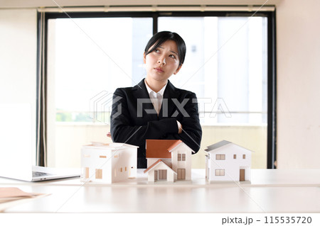 住宅模型の前で考えるスーツ姿の悩む女性 住宅模型の前で考えるスーツ姿の悩む女性 115535720