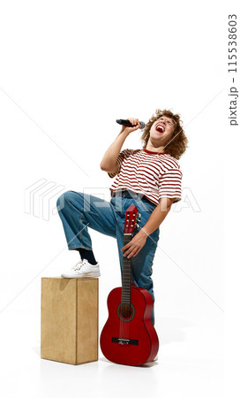 Full-length portrait of emotional young man, musician in jeans and striped shirt, staying with guitar an singing isolated on white background Full-length portrait of emotional young man, musician in jeans and striped shirt, staying with guitar an singing isolated on white background 115538603